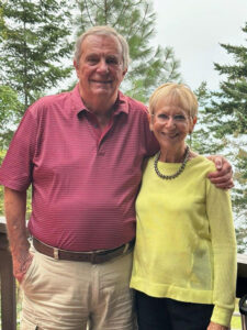 Co-Owner Greg Johnston and wife standing with green foliage in the background.