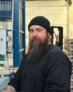 Photo of Sean working in the brewery with equipment in the background.